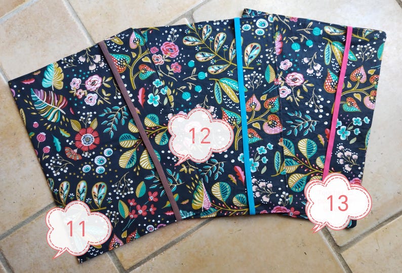 May include: Three fabric-covered notebooks with floral patterns in navy, pink, teal, and gold. Each notebook has a different colored elastic band: brown, teal, and pink. Numbers 11, 12, and 13 are on the notebooks.