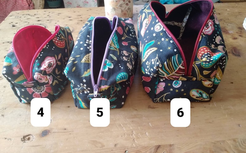 May include: Three fabric cosmetic bags with floral and leaf patterns on a black background. The bags have different colored zippers and interior linings. The bags are labeled with the numbers 4, 5, and 6.