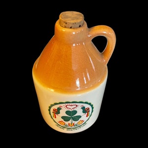 May include: A small ceramic jug with a cork stopper. The jug is decorated with a green shamrock, two birds, and the text "Irish Distelfink".