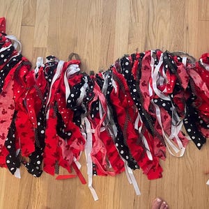 Puede incluir: Una guirnalda decorativa de tela compuesta por tiras de tela en rojo, negro y blanco. Los patrones incluyen colores s&oacute;lidos, lunares blancos sobre negro y peque&ntilde;as siluetas de personajes rojos impresas en tela roja, atadas a un cord&oacute;n.