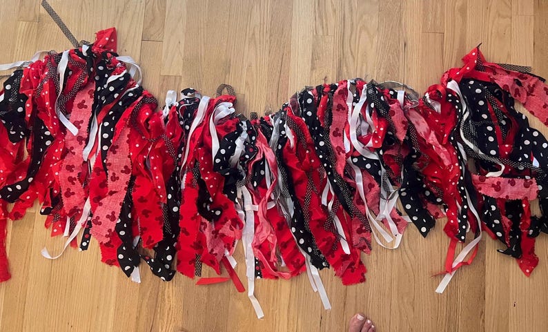 Puede incluir: Una guirnalda decorativa de tela compuesta por tiras de tela en rojo, negro y blanco. Los patrones incluyen colores s&oacute;lidos, lunares blancos sobre negro y peque&ntilde;as siluetas de personajes rojos impresas en tela roja, atadas a un cord&oacute;n.