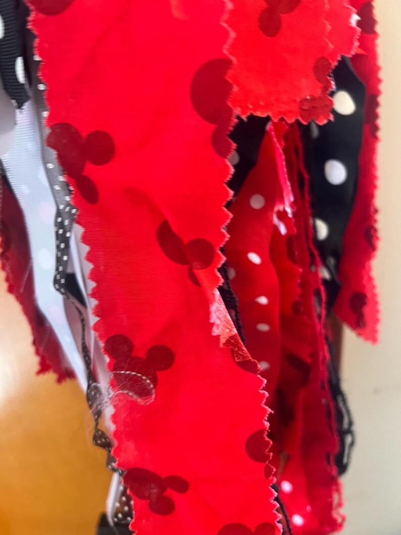 Puede incluir: Una colecci&oacute;n de tiras de tela con un fondo rojo y siluetas de cabezas de Mickey Mouse en rojo oscuro, intercaladas con tiras de tela negra decoradas con lunares blancos. Los bordes de la tela tienen un acabado dentado y recortado.