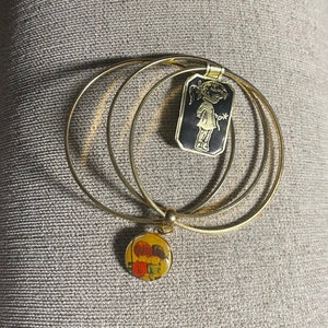 May include: A set of three gold bangle bracelets with two charms. One charm is a round image of two children, the other is a rectangular image of a girl in a dress.