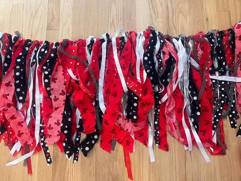 Puede incluir: Una guirnalda de tela con tiras rojas, negras y blancas. La tela incluye colores s&oacute;lidos en rojo, negro y blanco, junto con patrones de lunares blancos sobre tela negra y peque&ntilde;as siluetas de rat&oacute;n rojas sobre tela de color rojo.