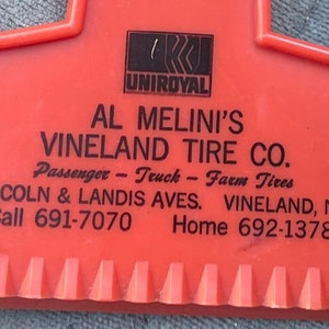 May include: Red plastic ice scraper with a black Uniroyal logo and the text "Al Melini's Vineland Tire Co. Passenger - Truck - Farm Tires Lincoln & Landis Aves. Vineland, N.J. Call 691-7070 Home 692-1378"
