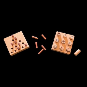 May include: A wooden game set with two boards and wooden pieces. One board has a triangular grid with holes and the other has a square grid with circles and crosses. The pieces are small wooden cylinders.