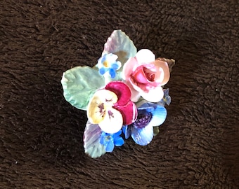 May include: A vintage porcelain flower brooch with a pink rose, purple and white pansies, blue forget-me-nots, and green leaves.
