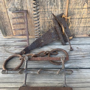 May include: A collection of antique rusty metal tools, including a rake, a chain, a spring, and a metal hook with a wooden handle.