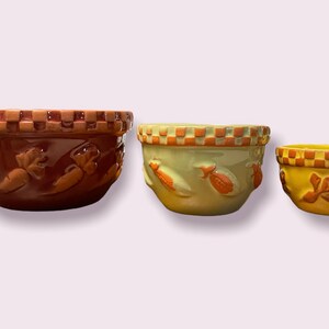 May include: Set of three ceramic mixing bowls with a checkered rim and embossed vegetable designs. The bowls are brown, green, and yellow.
