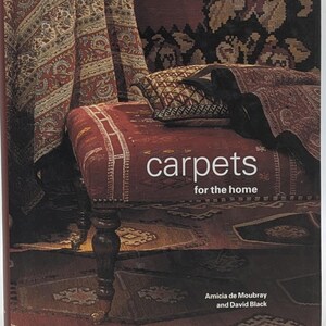 May include: A book titled "carpets for the home" by Amica de Moubray and David Black. The cover features a close-up of a red and brown patterned rug with a wooden stool and a throw pillow.
