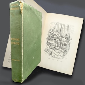 May include: A vintage hardcover book titled "Captain's Courageous" by Rudyard Kipling. The book has a green cover with gold lettering and is open to a black and white illustration of a ship and crew. The book is a "Century Edition".