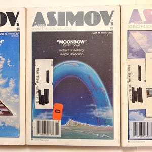 May include: Three vintage issues of Asimov's Science Fiction Magazine. The covers feature colorful illustrations and text, including titles like "Unicorn Variation" and "Moonbow." The magazines are displayed side by side.