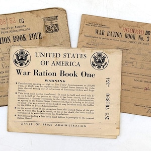 May include: Three vintage War Ration Books from the United States, including Book One, Book Three, and Book Four. The books are tan with black text and feature the official seal of the United States. The text includes warnings and instructions from the Office of Price Administration.