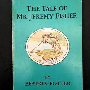 May include: A white ceramic mug with a black handle and the text "But First, Coffee" in a bold, black font. The mug is set against a blurred background, suggesting a cozy setting. The mug appears to be approximately 4 inches tall.