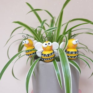 May include: Three yellow and black bumblebees with white wings are sitting in a pot of green and white striped spider plant.