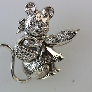 Peut inclure: Une figurine de souris en argent tenant un panier et une assiette de biscuits. La souris porte une robe et a un nœud sur la tête.
