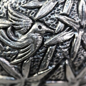 May include: Close-up of a silver metal ornament with a detailed design of birds and leaves.
