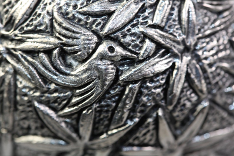 May include: Close-up of a silver metal ornament with a detailed design of birds and leaves.