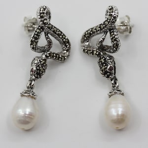 May include: A pair of silver snake earrings with marcasite and a pearl drop. The snakes are coiled and have a red gemstone in the eye.