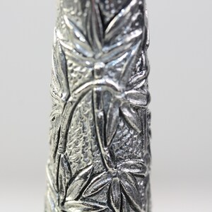 May include: Close-up of a silver metal vase with a detailed embossed design of leaves and flowers.
