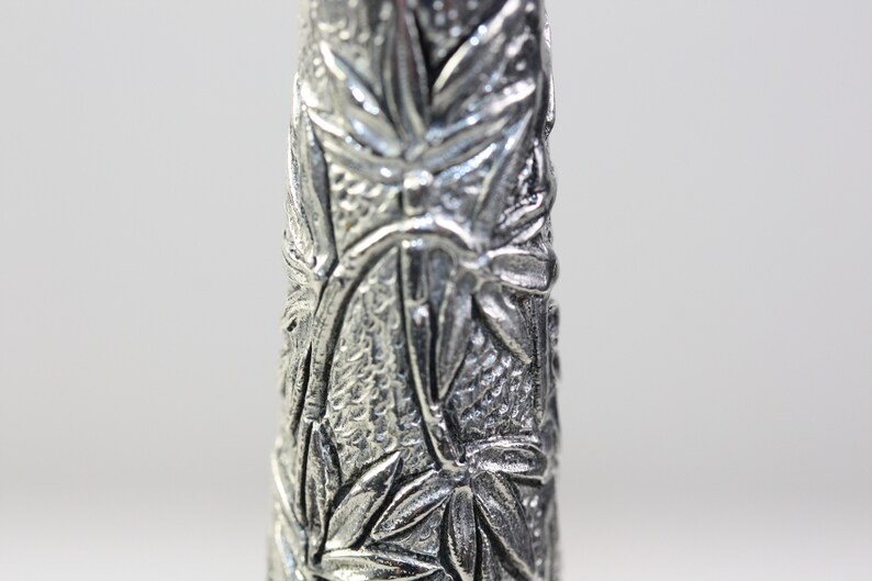 May include: Close-up of a silver metal vase with a detailed embossed design of leaves and flowers.