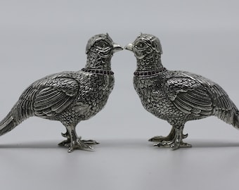 May include: A pair of silver pheasant salt and pepper shakers with red gemstone accents. The pheasants are facing each other with their tails extended.