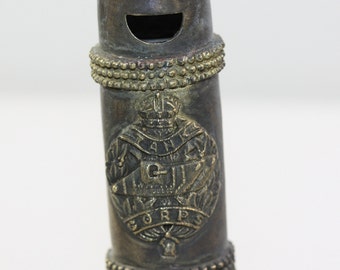 May include: A brass whistle with a decorative design featuring a crown and the word "CORPS".