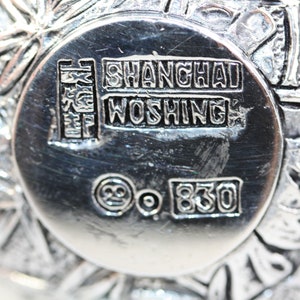 May include: Close-up of the bottom of a silver bowl with the inscription "SHANGHAI WOSHING" and the mark "925 830".