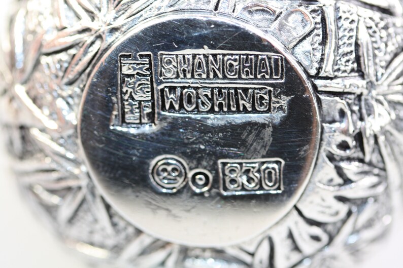 May include: Close-up of the bottom of a silver bowl with the inscription "SHANGHAI WOSHING" and the mark "925 830".