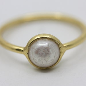 Puede incluir: Un anillo de oro con una perla blanca engastada en un engaste de oro.