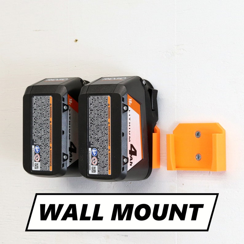 May include: Two black and orange 18v lithium-ion batteries with a 4Ah capacity mounted on a wall with an orange plastic wall mount. The text "WALL MOUNT" is printed below the batteries.