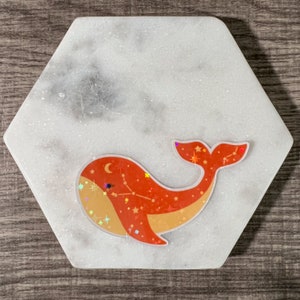 May include: A red and orange whale with a constellation design and glitter accents on a white marble background.