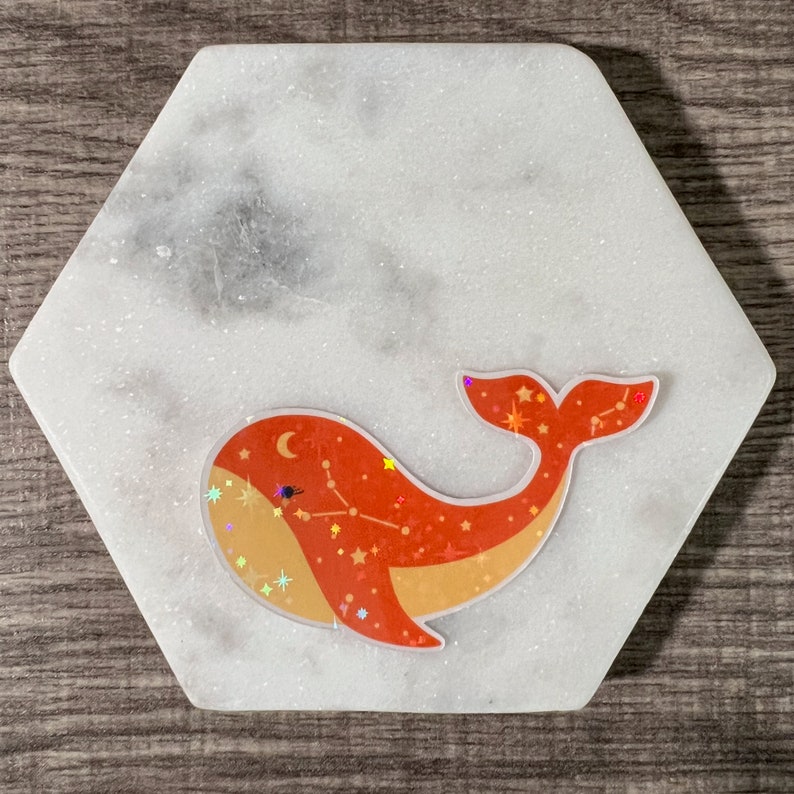 May include: A red and orange whale with a constellation design and glitter accents on a white marble background.