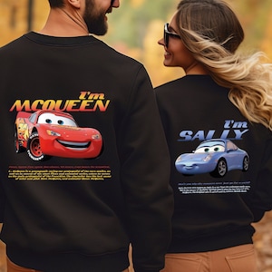 May include: A couple wearing black sweatshirts with a graphic print of the characters Lightning McQueen and Sally from the Disney Pixar movie Cars. The man's sweatshirt says "I'm McQueen" and the woman's sweatshirt says "I'm Sally".