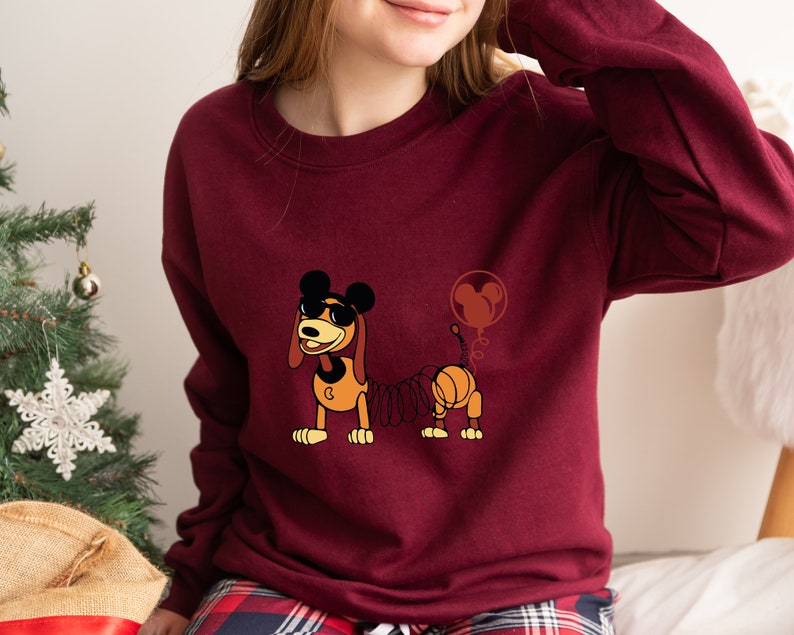 May include: A maroon sweatshirt with a cartoon image of a dog wearing sunglasses and a Mickey Mouse balloon. The dog is a spring-loaded toy with a coiled spring tail.