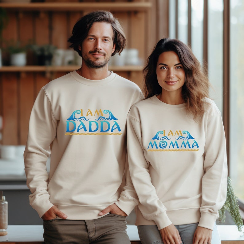 May include: Two cream colored sweatshirts with a blue and gold graphic design. The text on the sweatshirts reads "I am Dadda" and "I am Momma".