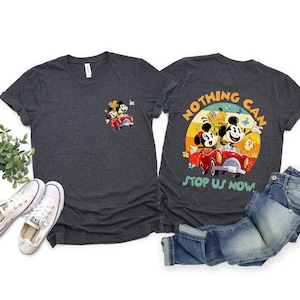 May include: Two dark gray t-shirts with a vintage-style graphic of Mickey Mouse, Minnie Mouse, and Pluto driving a red car. The graphic on the back of one shirt says "Nothing Can Stop Us Now!"