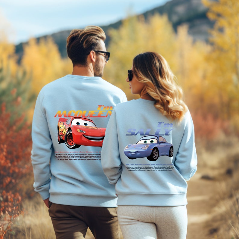 May include: A couple wearing light blue sweatshirts with a graphic print of the characters Lightning McQueen and Sally from the Disney Pixar movie Cars. The text on the sweatshirts reads "I'm McQueen" and "I'm Sally".