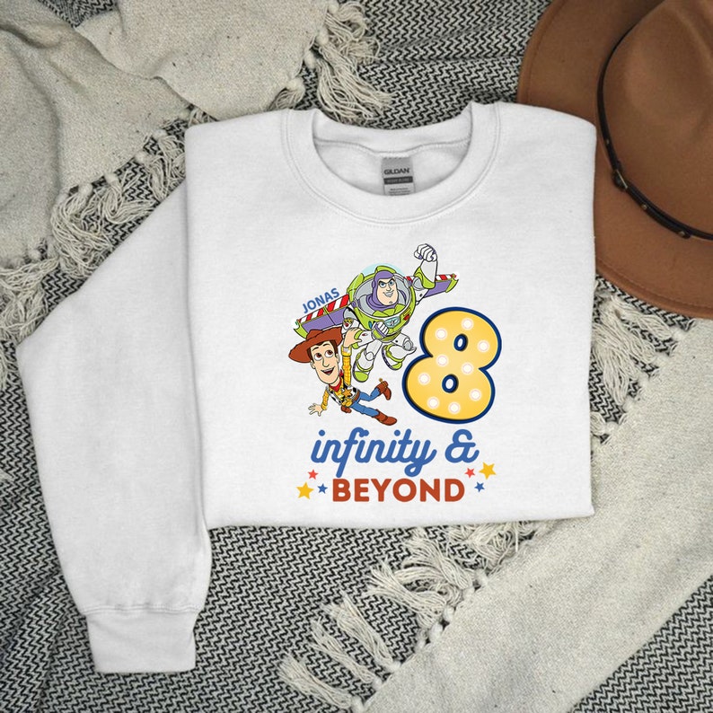 Puede incluir: Sudadera blanca con un gr&aacute;fico de Woody y Buzz Lightyear de Toy Story. El gr&aacute;fico incluye el n&uacute;mero 8, estrellas y el texto "infinity & beyond". El nombre "Jonas" est&aacute; impreso sobre el gr&aacute;fico.