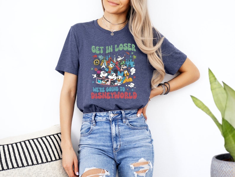Puede incluir: Una camiseta azul marino con un gr&aacute;fico de Mickey Mouse y sus amigos frente al castillo de Disney World. El texto en la camiseta dice "Get in loser, we're going to Disney World".