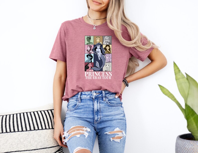 Puede incluir: Una camiseta rosa con un gr&aacute;fico de varias princesas Disney en cuadrados coloridos. El texto "Princess The Eras Tour" est&aacute; impreso debajo del gr&aacute;fico.