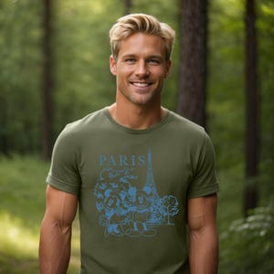 Op de afbeelding: Een groen T-shirt met een blauwe afbeelding van Mickey Mouse en Minnie Mouse voor de Eiffeltoren. De tekst "PARIS" staat boven de afbeelding.