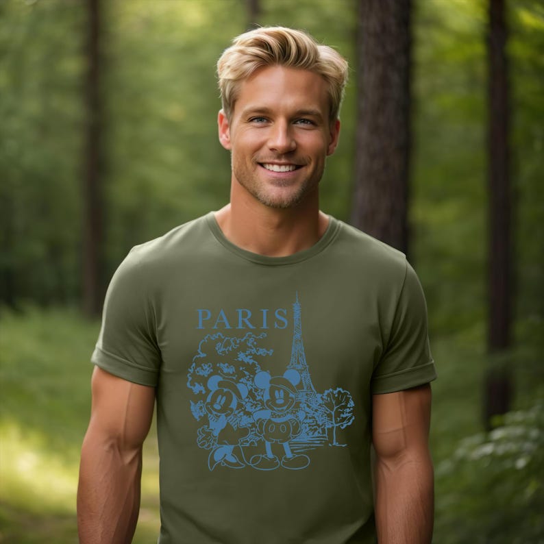 Op de afbeelding: Een groen T-shirt met een blauwe afbeelding van Mickey Mouse en Minnie Mouse voor de Eiffeltoren. De tekst "PARIS" staat boven de afbeelding.