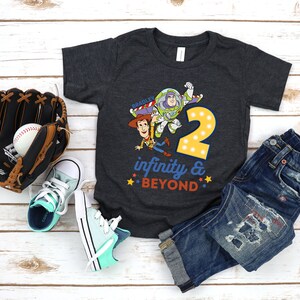 Puede incluir: Una camiseta gris oscuro con un gr&aacute;fico de Woody y Buzz Lightyear de Toy Story. El gr&aacute;fico incluye el n&uacute;mero 2 y el texto "infinito y m&aacute;s all&aacute;".