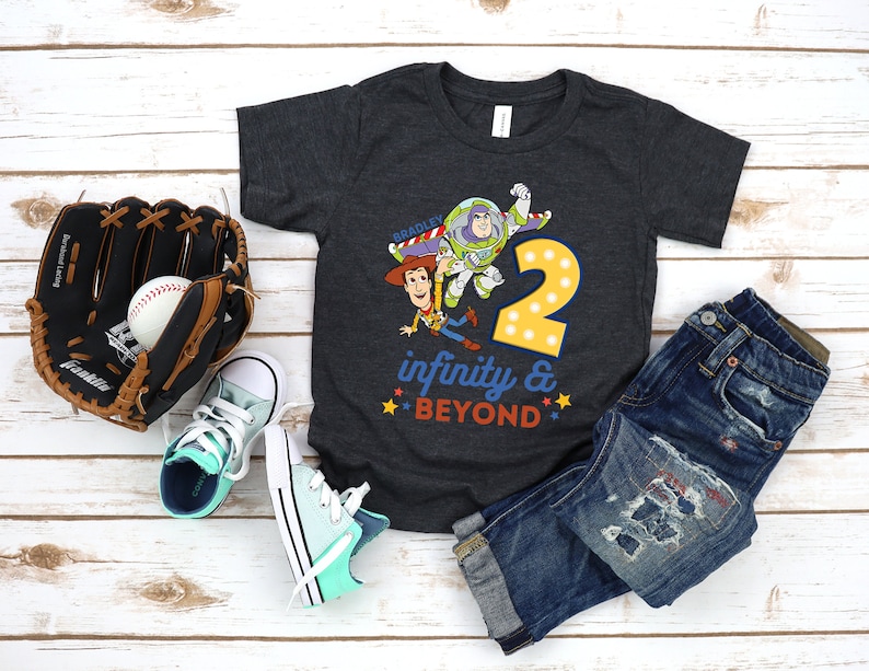 Puede incluir: Una camiseta gris oscuro con un gr&aacute;fico de Woody y Buzz Lightyear de Toy Story. El gr&aacute;fico incluye el n&uacute;mero 2 y el texto "infinito y m&aacute;s all&aacute;".