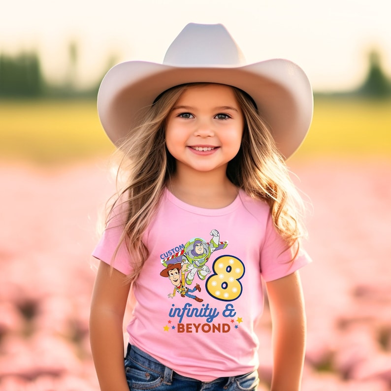 Puede incluir: Camiseta rosa con un gr&aacute;fico de Woody y Buzz Lightyear de Toy Story. La camiseta tiene un gran n&uacute;mero 8 con el texto "infinity & BEYOND" debajo.