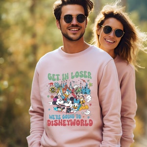 Puede incluir: Una sudadera rosa con un estampado gr&aacute;fico de Mickey Mouse y otros personajes de Disney. El texto en la sudadera dice "Get in loser, we're going to Disney World."