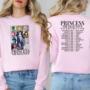 Puede incluir: Sudadera rosa con un gr&aacute;fico de princesas Disney en la parte delantera y una lista de princesas y sus fechas de estreno de pel&iacute;culas en la parte posterior. El texto en la parte delantera dice "Princess The Eras Tour". El texto en la parte posterior dice "Princess The Eras Tour".