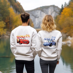 May include: White crewneck sweatshirts with a graphic print of Lightning McQueen and Sally from the movie Cars. The text "I'm McQueen" and "I'm Sally" is printed on the back of the sweatshirts.