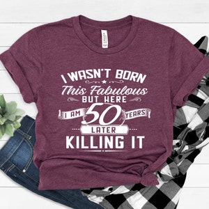 May include: A maroon t-shirt with white text that reads "I wasn't born this fabulous but here I am 50 years later killing it".